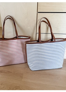 Detail showing large striped canvas tote bags in red and blue with brown leather handles