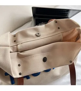 Detail of the magnetic buckle closure and brown leather handles on a canvas tote bag
