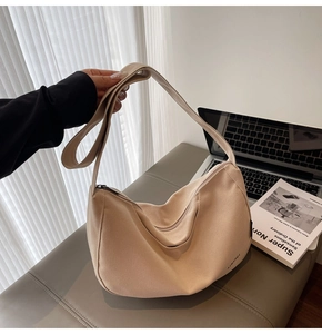 Detail der minimalistischen beigen Segeltuch-Sichel-Tasche mit Logo und Metallreißverschluss