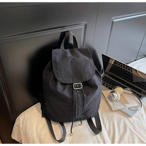 Sac à dos noir minimaliste imperméable avec cordon de serrage et ordinateur sur lit blanc