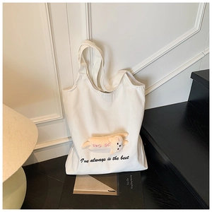 Detail of white canvas tote bag with black typography and cute plush cat pendant