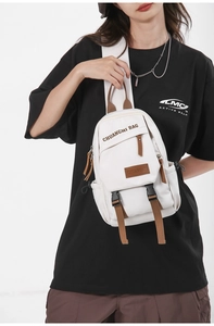 Close-up of white canvas chest bag featuring a brand patch and brown leather zipper pulls