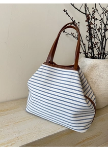 Detailed view of striped canvas tote bag with brown leather handles on marble surface