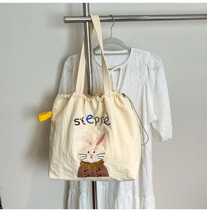 Detail of cute rabbit embroidery and steppe text on cream canvas drawstring tote bag