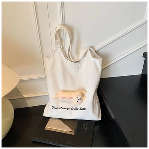 Detail of canvas tote bag with pink plush bear charm and cursive text embroidery
