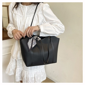 Detail of a black pebbled leather tote bag with a geometric silk scarf on the handle
