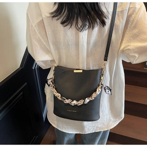 Détail du sac seau noir en cuir grainé avec foulard floral et bandoulière chaîne dorée
