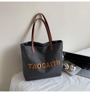 Close-up of a large canvas tote bag with leather handles and metallic letter logo detail