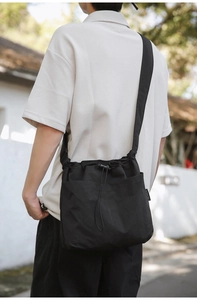 Detail of black nylon bucket bag with drawstring closure and brand label in outdoor setting