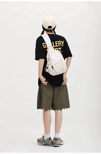 Detail of a creamy white nylon crossbody chest bag featuring a gold letter C logo on a model