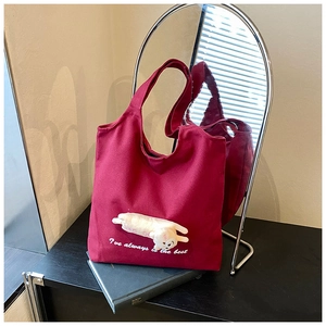 Detail of burgundy canvas tote bag featuring a 3D plush cat and white handwritten text