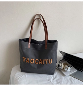 Detail of dark gray canvas tote with TAOCAITU embroidery and brown leather handles