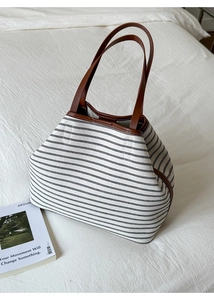 Detail of striped canvas tote bag with brown leather handles and stitching on white fabric