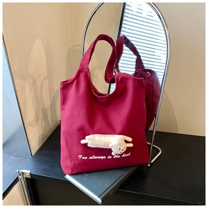 Detail of burgundy canvas tote bag featuring 3D plush cat and white embroidered quote