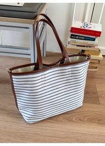 Detail of striped canvas tote bag showing dark brown leather handles and golden metal rings