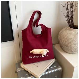 Detail of burgundy canvas tote with beige bear plush and white printed text on luggage