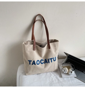 Detail of canvas tote bag with blue embroidered text and brown leather shoulder straps