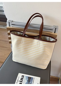 Detail of yellow striped canvas tote bag with brown leather handle on a grey chair