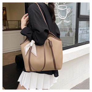 Detail of khaki tote bag with dark brown trim and plaid silk scarf on the handle
