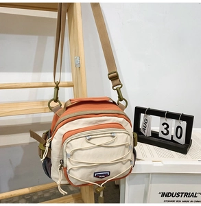Detail of orange and beige crossbody bag featuring adjustable strap and multi-pocket layout