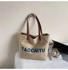 Detail of canvas tote bag featuring blue embroidery and brown leather handles in a home office