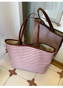 Detail view of large red striped canvas tote bag with brown leather handles and zipper