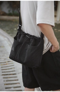 Detail of a black nylon drawstring bucket bag with large front pockets on a model