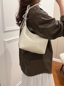 Sac sous le bras en cuir blanc crème avec grand nœud porté par un mannequin élégant