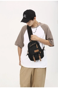 Detail of black crossbody sling bag with brown zipper tabs on male model