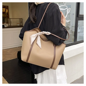 Detail of khaki tote bag with dark brown trim and stylish silk scarf tied on handle