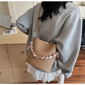 Sac seau marron avec poignée en chaîne et foulard en soie dans un cadre de bureau décontracté
