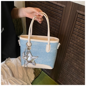 Détail d'un sac cabas en denim bleu avec finitions en cuir crème et pendentif étoile
