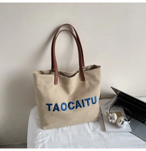 Close-up of beige canvas tote bag with blue 3D embroidery and brown leather straps