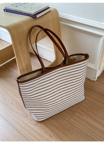 Detail of canvas tote bag with blue stripes, brown leather handles and contrast stitching