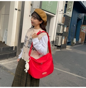 Detail of red nylon crescent bag with adjustable strap and cute cartoon chicken charm