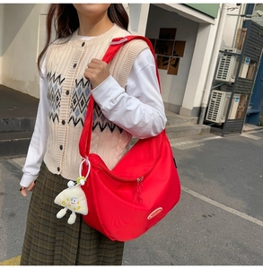 Detail of red nylon crossbody bag with wide strap and cute plush charm in outdoor use