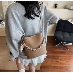 Detail of khaki leather bucket bag with silk scarf metal chain on a model