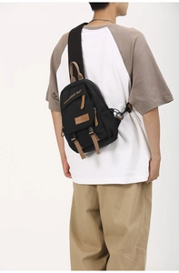 Rear view of model wearing black canvas sling bag with multiple zip pockets and brown trim