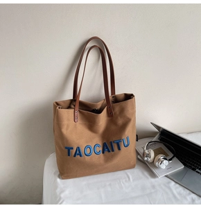 Detailed close-up of brown canvas tote bag with blue TAOCAITU embroidery and leather handles