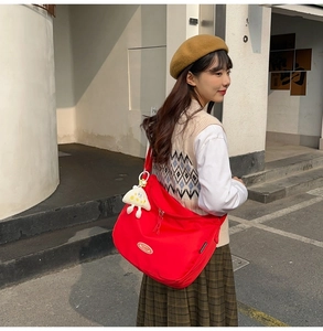 Detail of red nylon crossbody bag with dual zippers and white plush charm on model