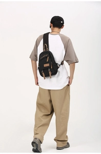 Detail of black canvas chest bag featuring brown leather accents and dual buckle closure