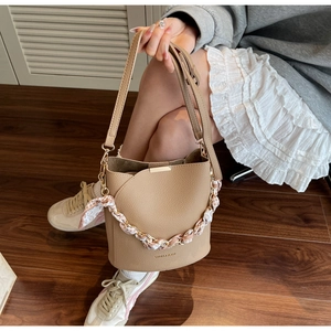 Détail du sac seau en cuir beige avec chaîne en métal ornée d'un foulard en soie
