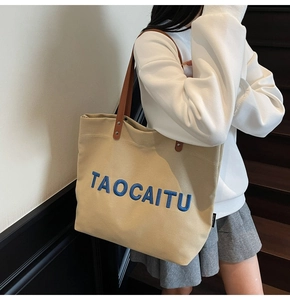 Canvas tote bag with blue embroidered letters and leather handles on model side view