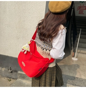 Detail of red nylon messenger bag with plush charm and wide strap on college-style model