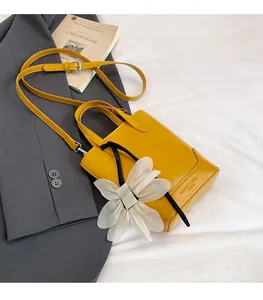 Detail der gelben Lederhandtasche mit weißem Chiffon-Blumenanhänger und verstellbarem Gurt