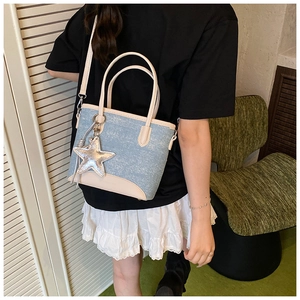 Détail du sac seau en denim bleu clair avec bordure en cuir beige et breloque étoile argentée