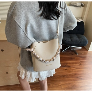 Détail du sac seau en cuir crème avec poignée en foulard et chaîne dorée