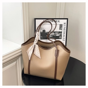 Detailed shot of beige leather tote bag with brown trim and floral scarf on a table