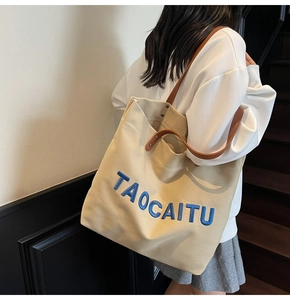 Detail of TAOCAITU beige canvas tote bag showing blue embroidery and brown leather strap