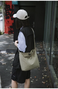 Detail of khaki nylon drawstring crossbody bag showing adjustable strap and side pocket